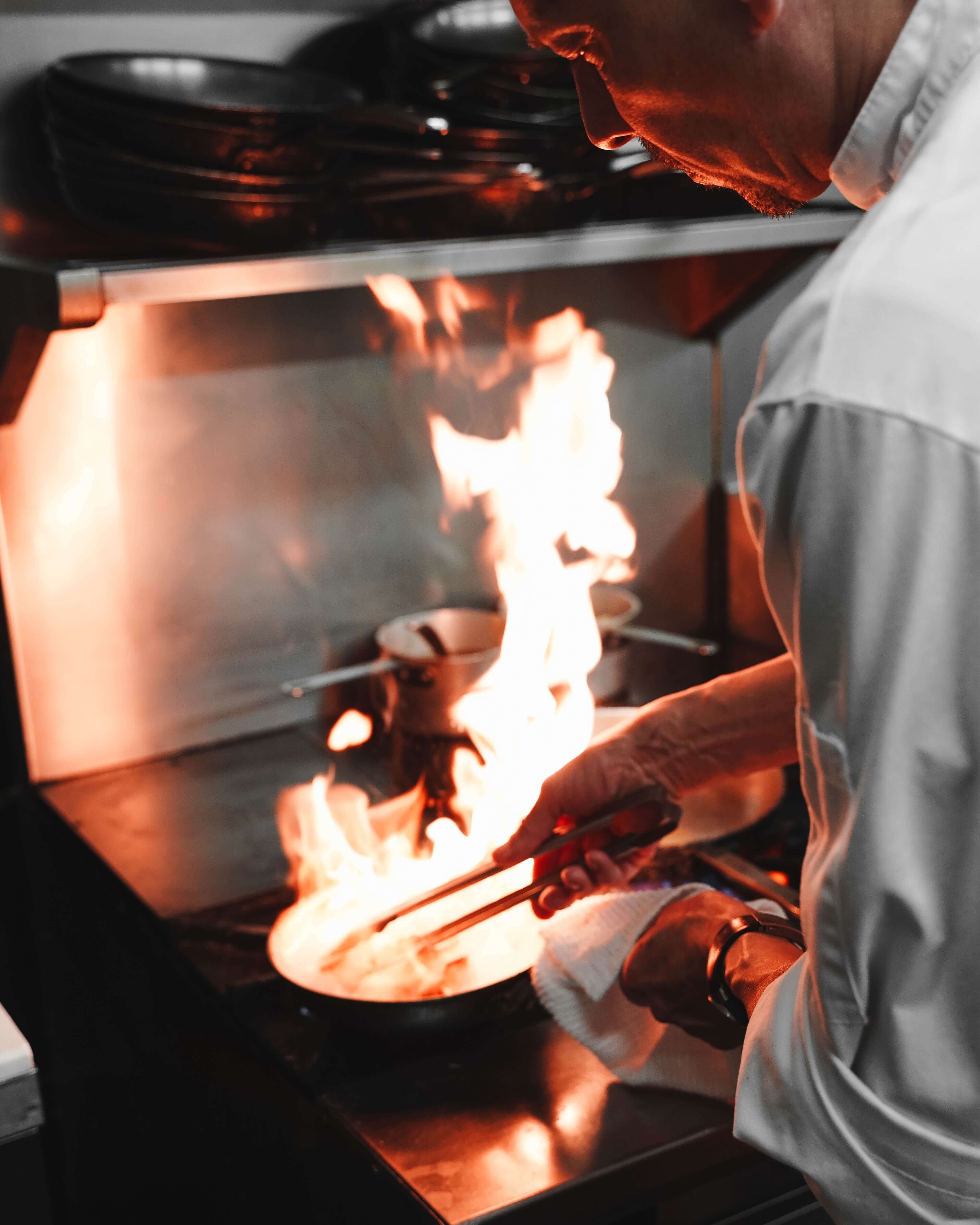 Pans stacked on the top of a range stove. Chef Ralphio preparing a dish in a skillet while flames engulf the contents